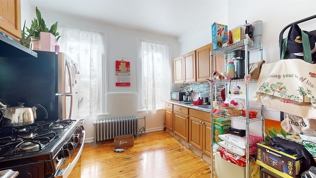 kitchen with radiator heating unit, backsplash, range with gas cooktop, stainless steel refrigerator, and light hardwood / wood-style flooring