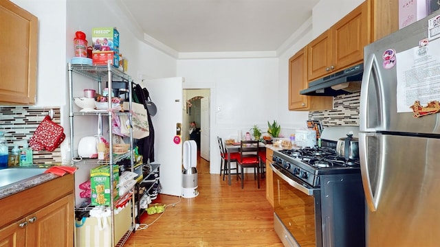 kitchen with appliances with stainless steel finishes, decorative backsplash, crown molding, and light hardwood / wood-style flooring