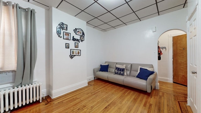 living room featuring a paneled ceiling, radiator heating unit, and light wood-type flooring