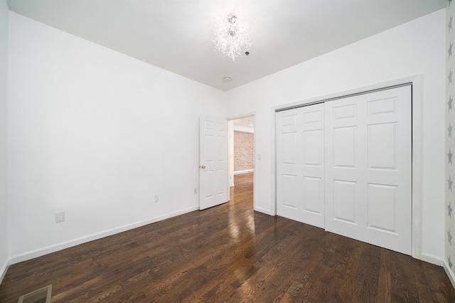 unfurnished bedroom featuring baseboards, visible vents, dark wood-style flooring, an inviting chandelier, and a closet