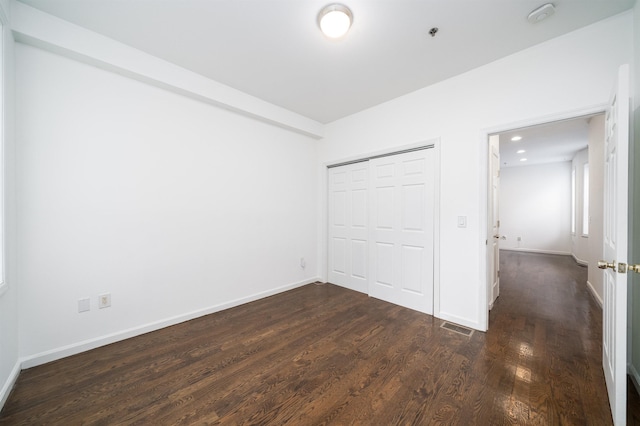 unfurnished bedroom featuring visible vents, baseboards, dark wood finished floors, and a closet