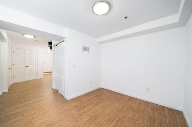 unfurnished room with light wood-type flooring, visible vents, baseboards, and a barn door