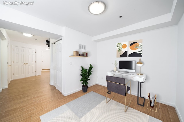 office space with a barn door, wood finished floors, visible vents, and baseboards