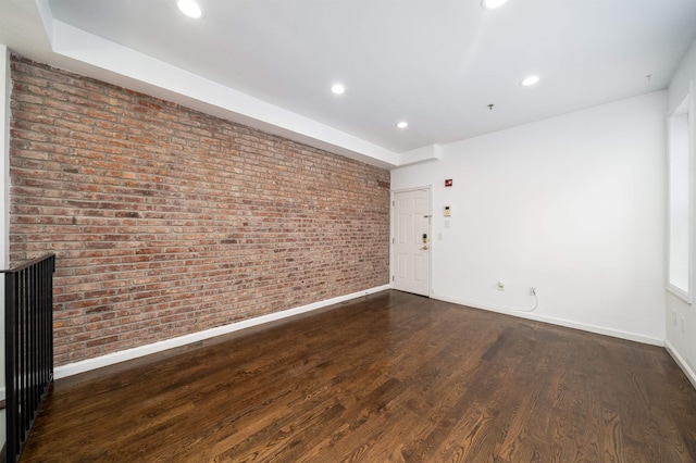 empty room with brick wall, baseboards, wood finished floors, and recessed lighting