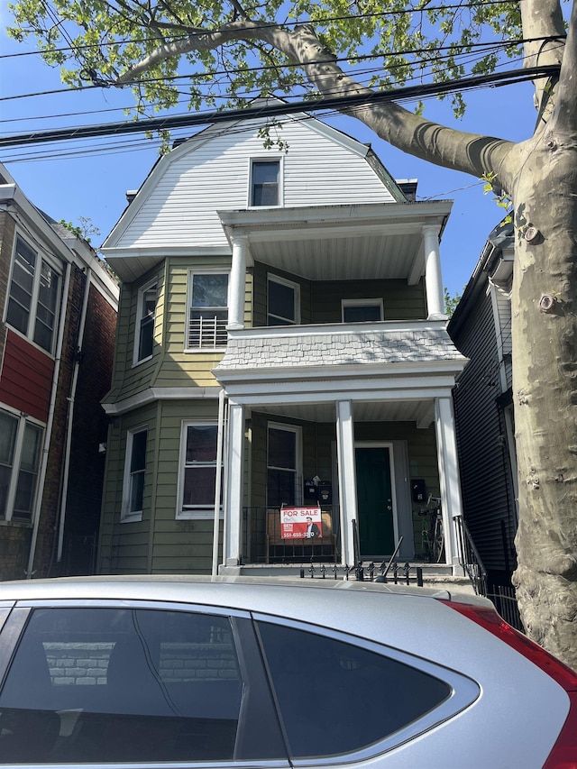 colonial inspired home featuring a balcony, a gambrel roof, and a porch