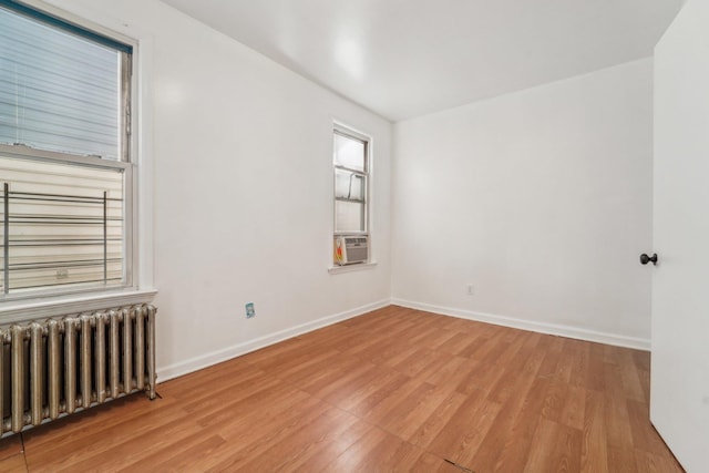 spare room featuring radiator heating unit, light wood-type flooring, and cooling unit