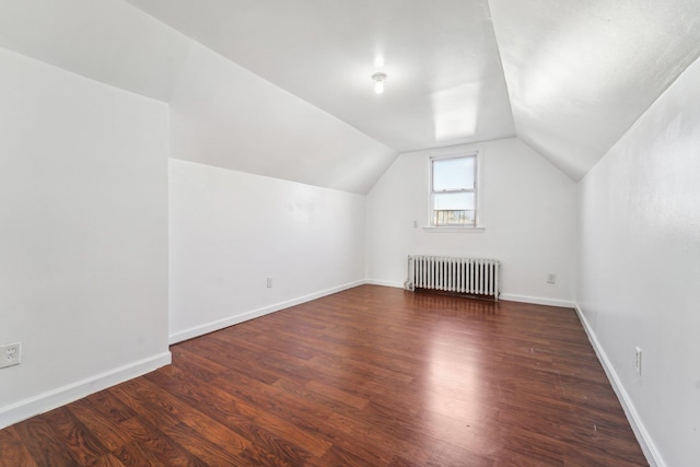 additional living space featuring vaulted ceiling, radiator, and dark wood-type flooring