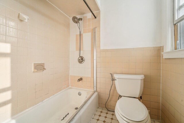 bathroom featuring tile patterned flooring, toilet, tile walls, and tiled shower / bath