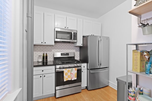 kitchen with light wood-style flooring, dark countertops, white cabinetry, appliances with stainless steel finishes, and decorative backsplash