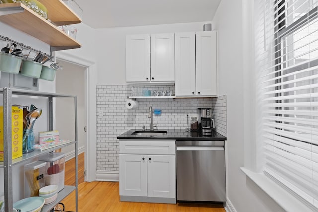 kitchen with stainless steel dishwasher, open shelves, dark countertops, and a sink