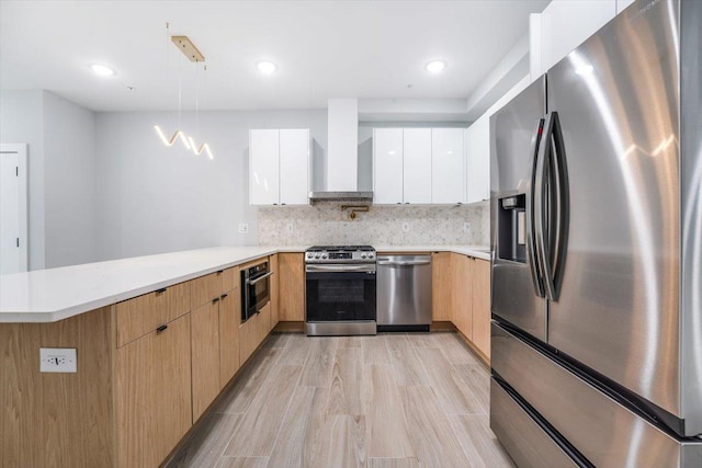 kitchen with appliances with stainless steel finishes, modern cabinets, a peninsula, wall chimney range hood, and light countertops