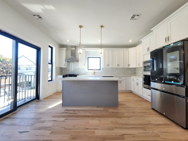 kitchen featuring white cabinets, a center island, wall chimney exhaust hood, decorative light fixtures, and light hardwood / wood-style floors