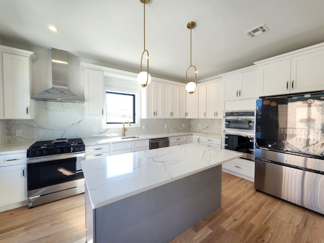 kitchen featuring white cabinets, appliances with stainless steel finishes, a kitchen island, decorative light fixtures, and wall chimney range hood