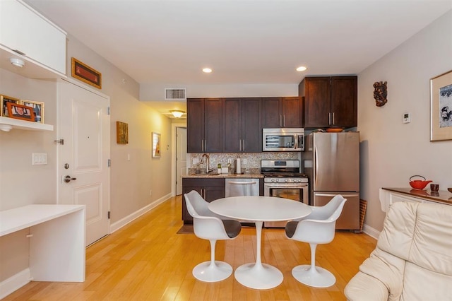 112 Liberty View Dr Unit 2A, Jersey City, NJ 07302 - kitchen featuring appliances with stainless steel finishes, decorative backsplash, light wood-type flooring, dark brown cabinets, and a breakfast bar area