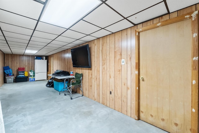 interior space featuring a drop ceiling, wood walls, and freestanding refrigerator