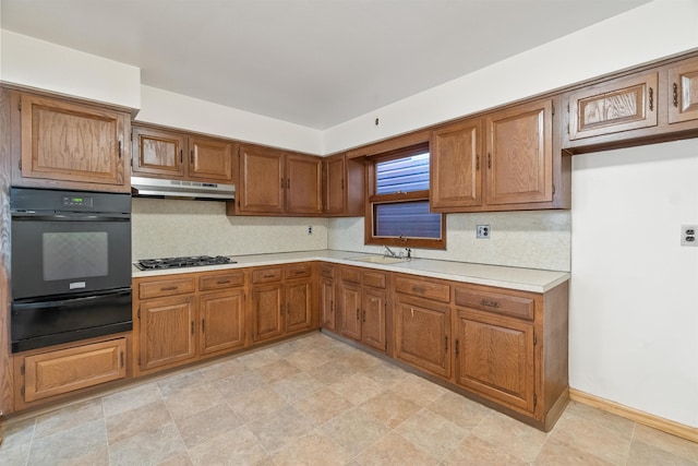 kitchen with oven, under cabinet range hood, a sink, brown cabinetry, and light countertops