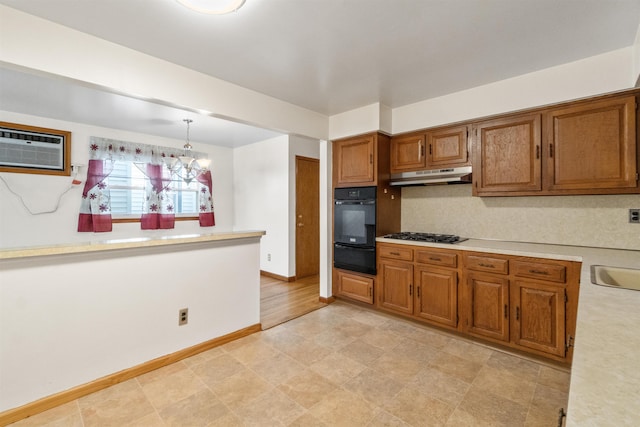 kitchen with under cabinet range hood, light countertops, brown cabinetry, a notable chandelier, and a wall mounted AC