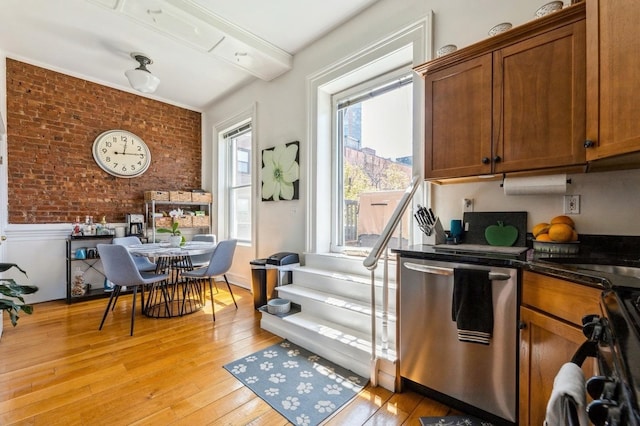 kitchen featuring brick wall, light hardwood / wood-style floors, stainless steel dishwasher, and dark stone counters