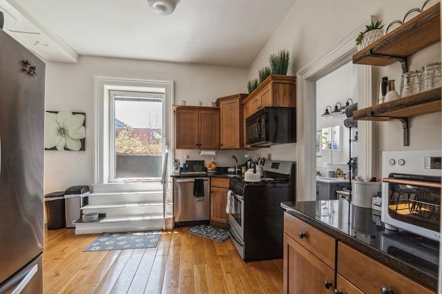 kitchen with sink, dark stone countertops, stainless steel appliances, and light wood-type flooring