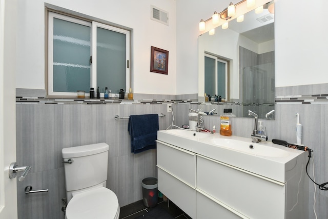 bathroom with tile walls, visible vents, vanity, and toilet