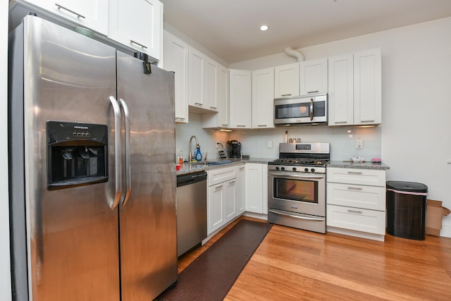 kitchen featuring white cabinets, decorative backsplash, light stone countertops, stainless steel appliances, and a sink