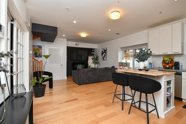 kitchen with light wood-style flooring, a breakfast bar, white cabinetry, stainless steel dishwasher, and recessed lighting