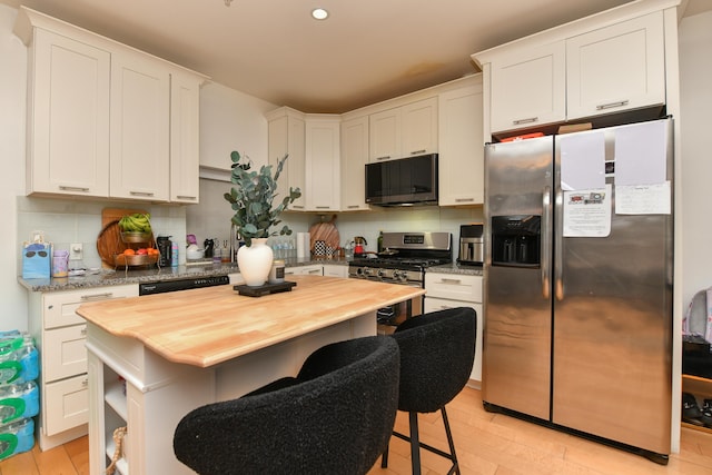 kitchen featuring appliances with stainless steel finishes, butcher block countertops, white cabinetry, and decorative backsplash