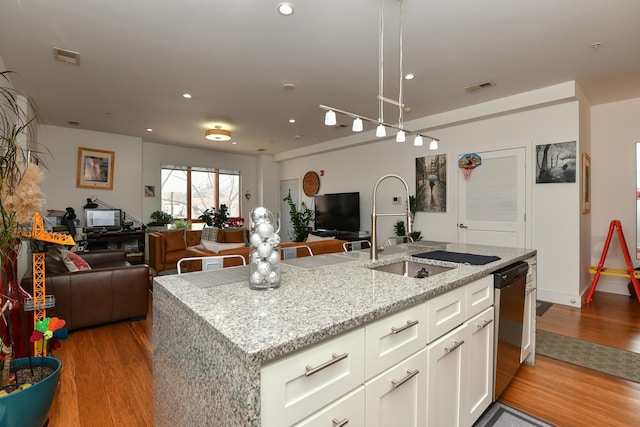 kitchen with light wood finished floors, visible vents, dishwasher, open floor plan, and a sink