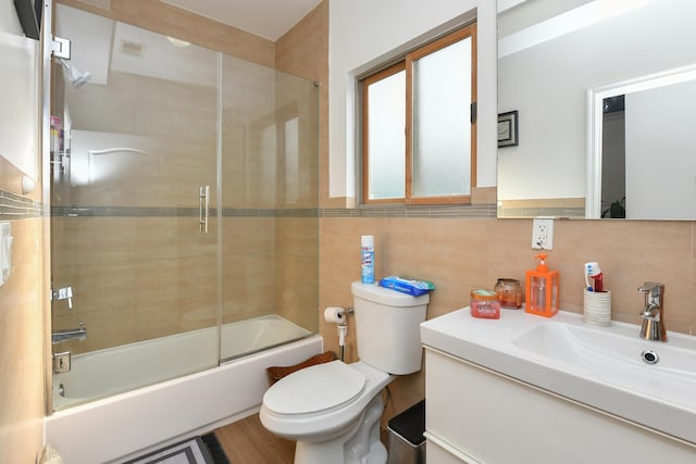 bathroom featuring visible vents, toilet, shower / bath combination with glass door, vanity, and tile walls