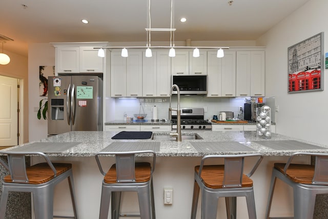 kitchen featuring pendant lighting, backsplash, appliances with stainless steel finishes, white cabinetry, and a kitchen breakfast bar