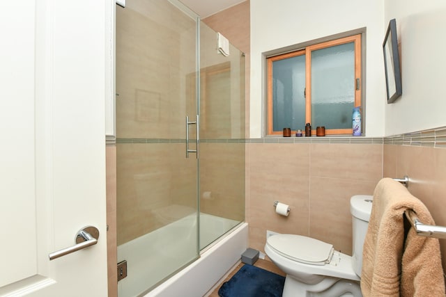 bathroom with toilet, enclosed tub / shower combo, and tile walls