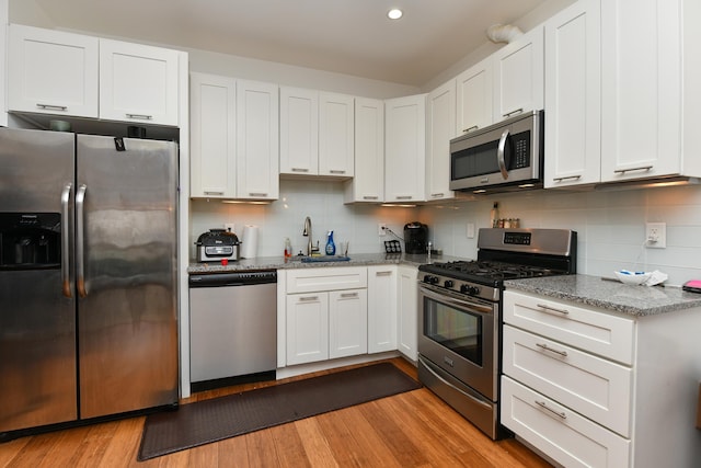 kitchen featuring light stone counters, stainless steel appliances, white cabinetry, a sink, and light wood-type flooring