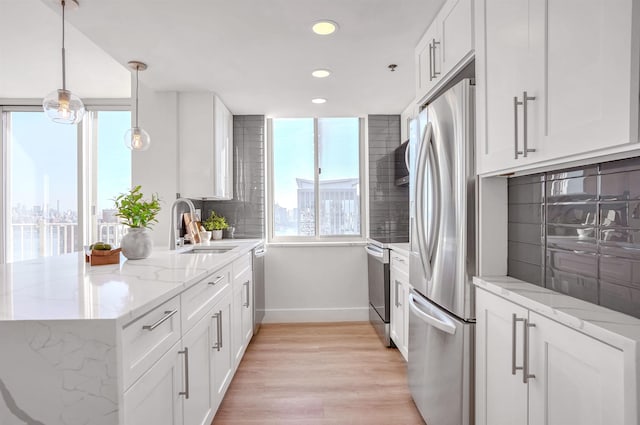 kitchen with light stone countertops, appliances with stainless steel finishes, pendant lighting, white cabinets, and light hardwood / wood-style floors