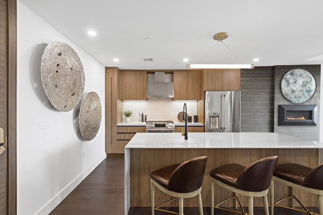 kitchen featuring high end appliances, a large fireplace, dark hardwood / wood-style flooring, kitchen peninsula, and wall chimney exhaust hood