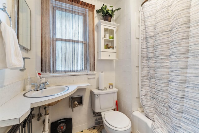 bathroom featuring tile walls, toilet, shower / bath combo with shower curtain, and a sink