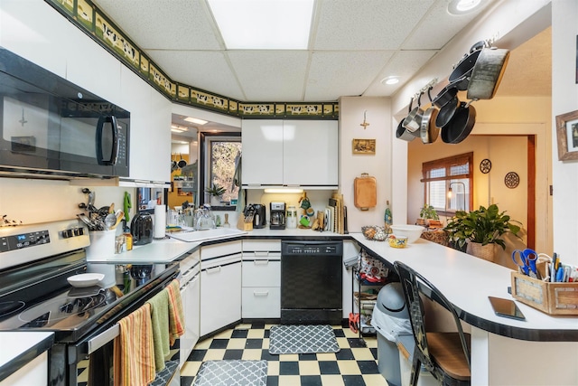 kitchen featuring tile patterned floors, black appliances, white cabinetry, a peninsula, and a paneled ceiling