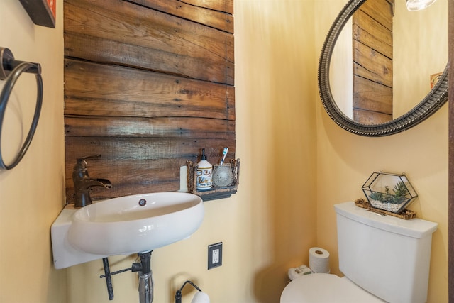 bathroom featuring wood walls, toilet, and a sink