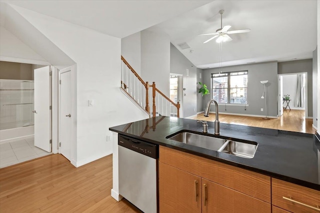 kitchen featuring a sink, vaulted ceiling, dishwasher, light wood finished floors, and dark countertops