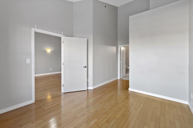 empty room featuring wood-type flooring, a high ceiling, and baseboards