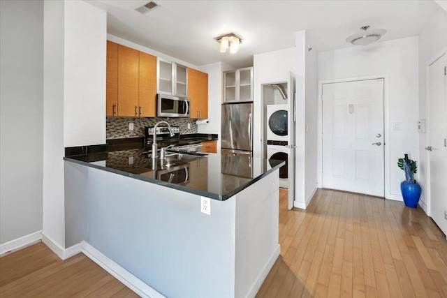 kitchen featuring stainless steel appliances, stacked washer and dryer, a peninsula, visible vents, and decorative backsplash