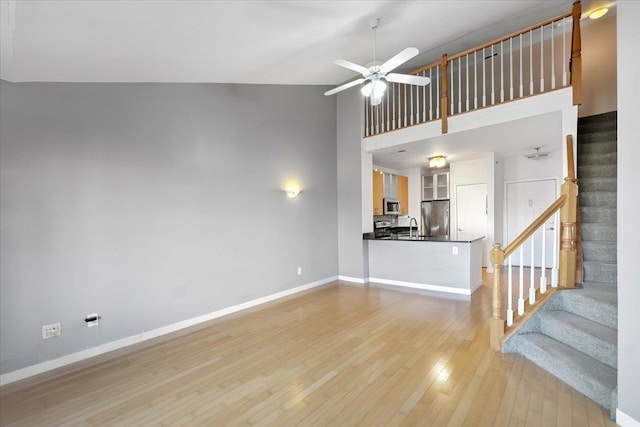 unfurnished living room featuring light wood finished floors, stairway, a sink, ceiling fan, and baseboards