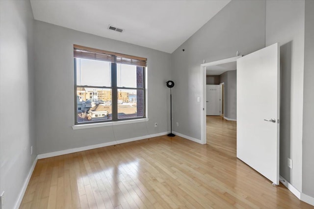 empty room featuring vaulted ceiling, visible vents, light wood-style flooring, and baseboards