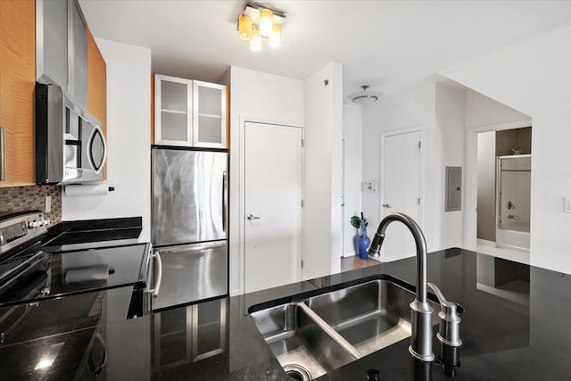 kitchen with decorative backsplash, appliances with stainless steel finishes, glass insert cabinets, a sink, and electric panel