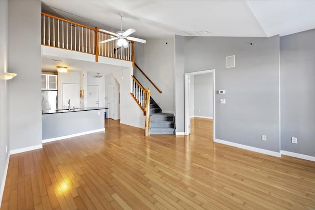 unfurnished living room featuring ceiling fan, high vaulted ceiling, hardwood / wood-style flooring, baseboards, and stairs