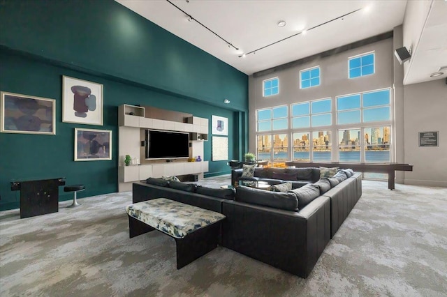 living room featuring rail lighting, baseboards, carpet flooring, and a high ceiling