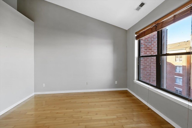 spare room with lofted ceiling, light wood finished floors, visible vents, and baseboards