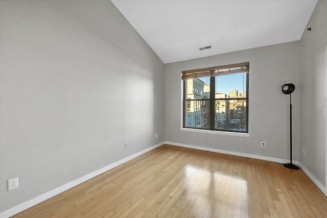 spare room with lofted ceiling, wood-type flooring, visible vents, and baseboards