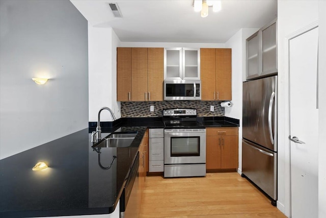 kitchen featuring light wood-style floors, appliances with stainless steel finishes, brown cabinets, and a sink