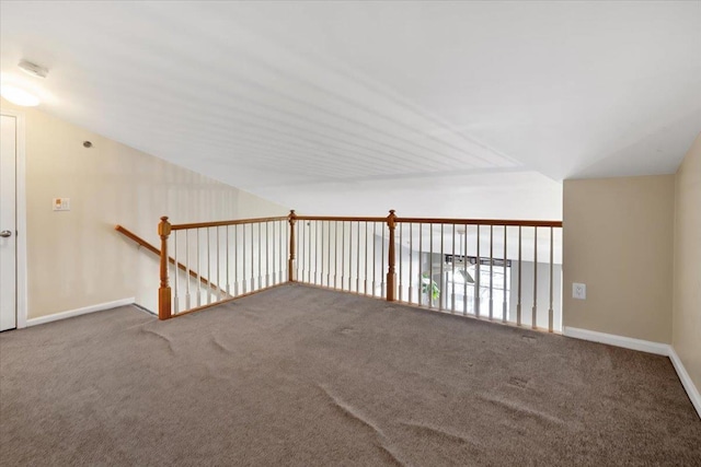 carpeted spare room featuring lofted ceiling and baseboards