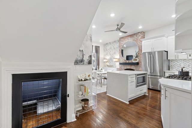 kitchen with a brick fireplace, white cabinets, backsplash, and appliances with stainless steel finishes